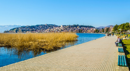 Wall Mural - people are strolling ona lakeside promenade next to the ohrid lake during sunny day in february.