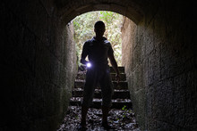 Young Man With A Flashlight Enters Stone Tunnel