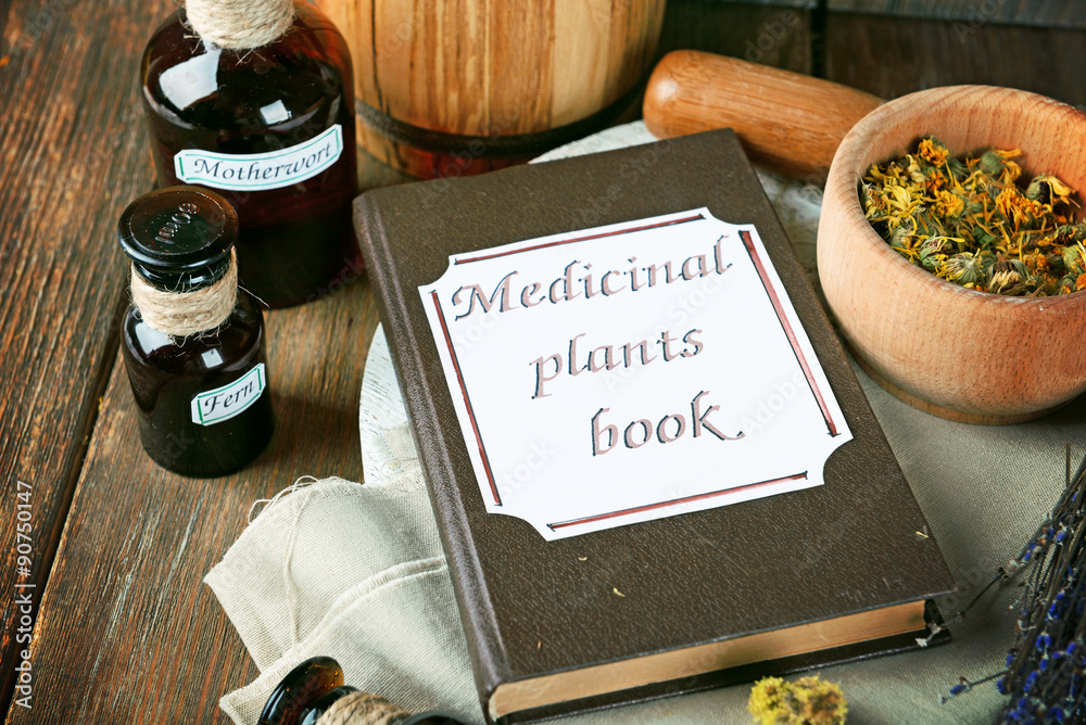 Medicinal plants book with dried herbs and bottles on table close up
