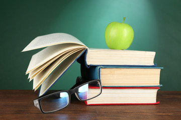 Poster - Stack of books, glasses and green apple on desk on green chalkboard background