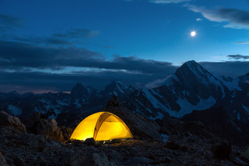 Wall Mural - Twilight Mountain Panorama and Tent Illuminated Camping Yellow Tent Night High Altitude Alpine Landscape Shining Moon in Dark Blue Sky cooler tone
