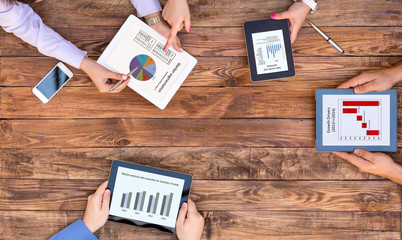 Business Brainstorming Session Hands of Business People Discussing Charts Data on Screens of Electronic Gadgets at Natural Plank Wood Desk