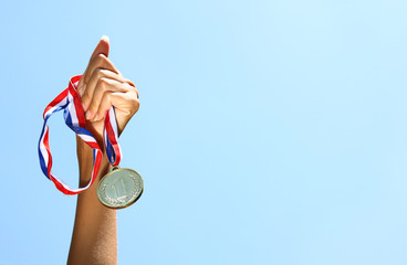 Wall Mural - woman hand raised, holding gold medal against skyl. award and victory concept