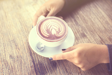 Wall Mural - Girl hands with cup of cappuccino on a wooden table, vintage pho