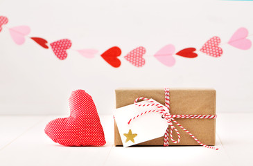 Wall Mural - A garland of hearts above a small gift-wrapped box and textile heart on a off white background