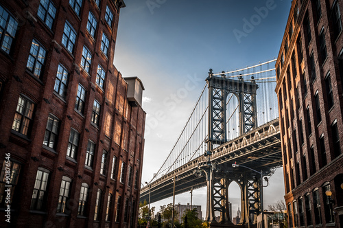 Plakat Manhattan most widzieć od wąskiej alei ogradzającej dwa ceglanymi budynkami na słonecznym dniu w lecie