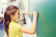 little smiling schoolgirl writing on chalk board
