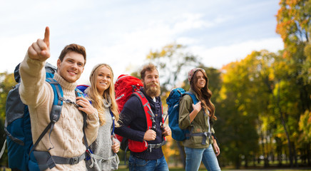 Canvas Print - smiling friends with backpacks hiking over nature