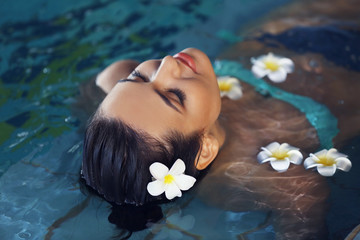 Beautiful young woman with flowers at swimming pool