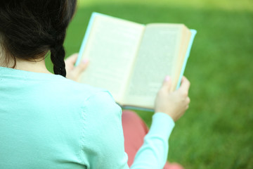 Wall Mural - Young woman with book sitting on green grass outdoors