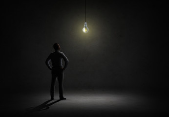 Poster - businessman looking at lighting bulb in dark room