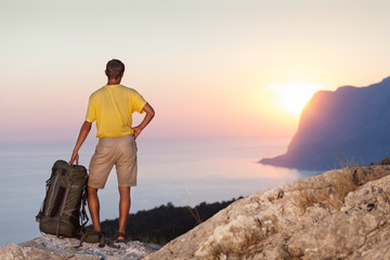 Man holds backpack and looking at sunrise