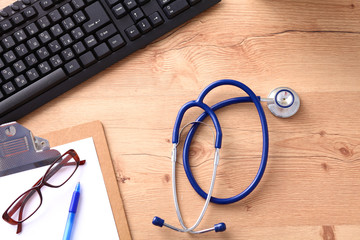 A medical stethoscope near a laptop on a wooden table, on white