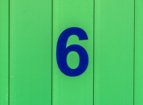 the number six, blue, set against bright green wood