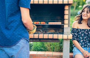 Man cooking sausages and vegetable skewers in a barbecue