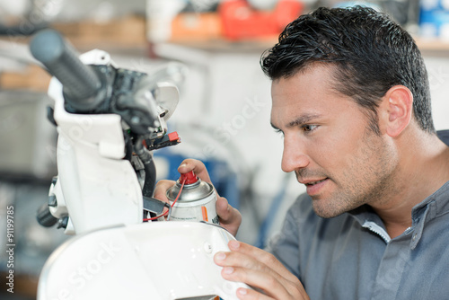 Fotografía Mechanic spraying lubricant on a scooter