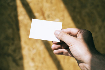 Closeup of hand holding white business card on the blurred wall 