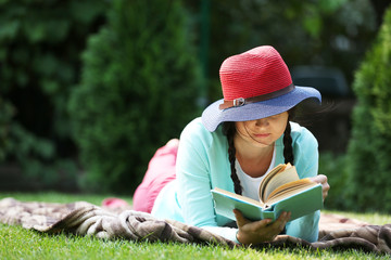 Wall Mural - Young woman with book lying on green grass outdoors