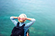© aboutmomentsimages - young woman on summer vacation, hiking on coastline and staring at sea wearing hat and backpack. Travel and adventure concept