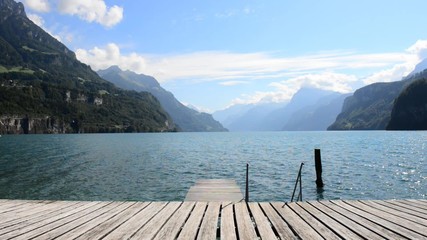 Wall Mural - Impressive mountain landscape, lake and clouds above. In the foreground a wooden pier. Alps in Europe.