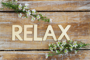 relax written on rustic wood and chamomile flowers