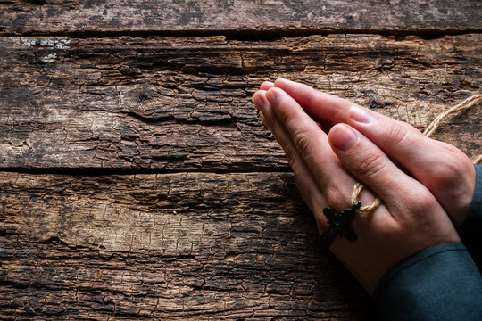 man praying with a cross in his hands on a wooden background