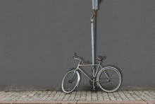 Old Fashioned Bicycle Attached With Lock To Pole With Road Sign And Gray Wall In Background