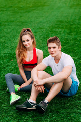 Wall Mural - Young athletic couple sitting on the grass