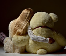 teenage girl sitting backward hugging big teddy bear back view