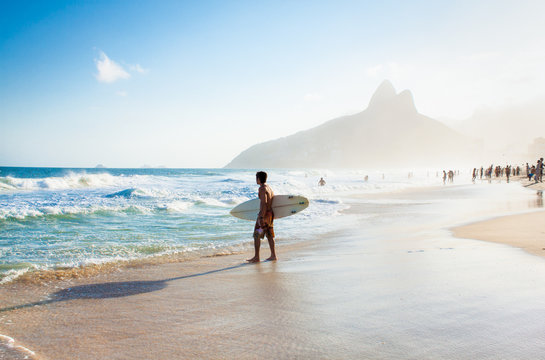 brazilian surfer walking with surfboard toward two brothers moun