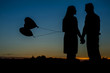Silhouette of an in love couple with 2 heart balloons. 