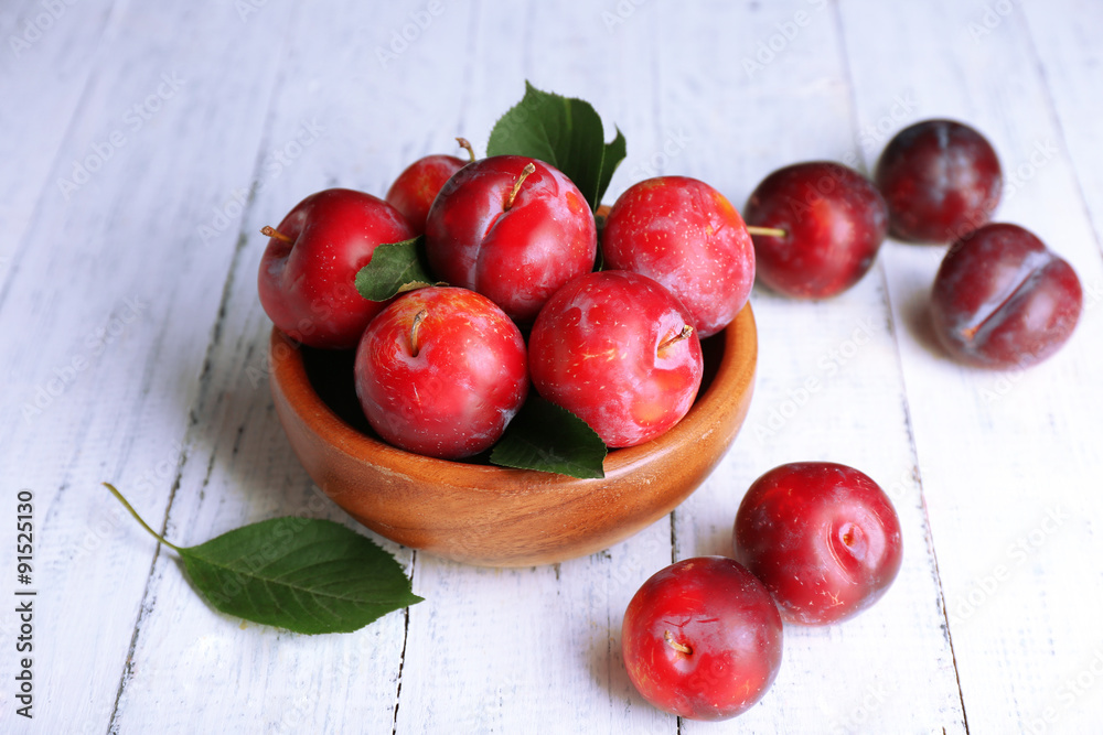 Ripe plums in bowl on wooden background