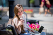 Young beautiful woman sitting on a bench with laptop and coffee in hand
