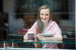 Young pretty woman with long hair drinking coffee and using tablet computer in cafe. Smiling and looking through the window

