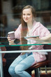 Young pretty woman with long hair drinking coffee and using tablet computer in cafe. Smiling and looking through the window
