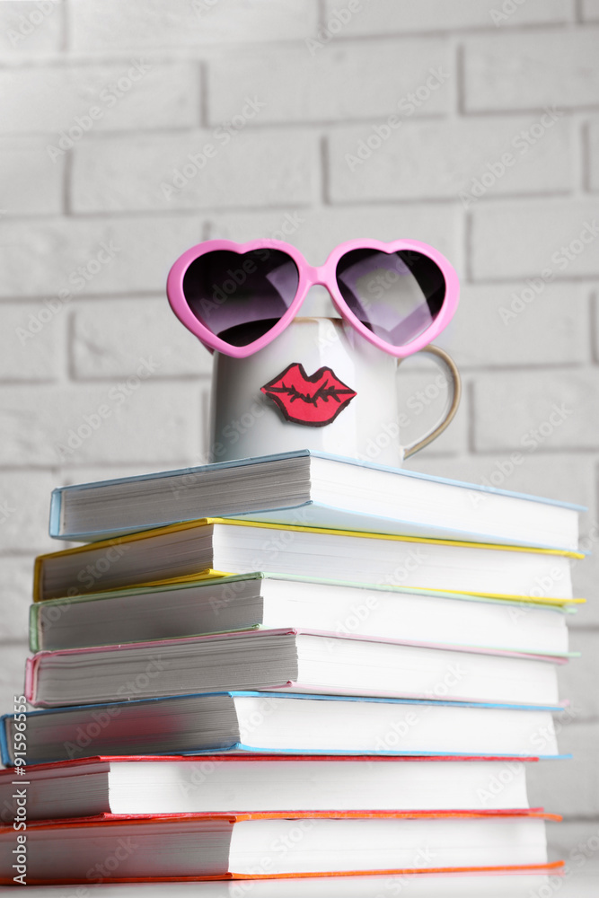 Books and cup with lips on wooden table on brick wall background
