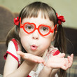 Cute little girl with glasses in the shape of a heart sends an air kiss