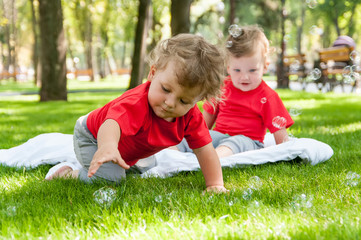 children twins play on the grass with soap bubbles