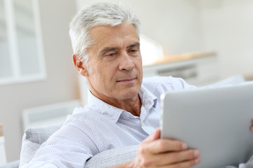 Senior man relaxing in sofa and using digital tablet