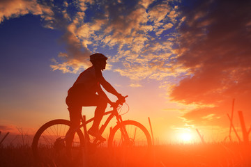 Wall Mural - Silhouette of a biker and bicycle on sky background.