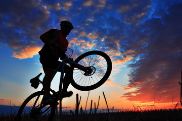 Wall Mural - Silhouette of a biker and bicycle on sky background.