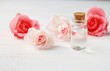 Pure rose water in glass bottle fresh pink pastel rose blossom delicate, spa beauty care setting, wooden shelf, soft focus