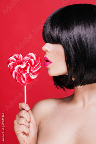 Fotografie, Obraz Closeup photo of a beautiful sexy pink lips with lollipop on red