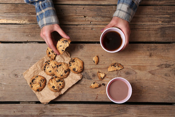 Canvas Print - Female hands holding cup of coffee and cookies on wooden table close up