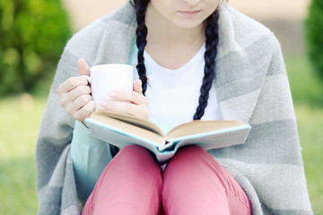 Wall Mural - Young woman with book sitting on green grass outdoors