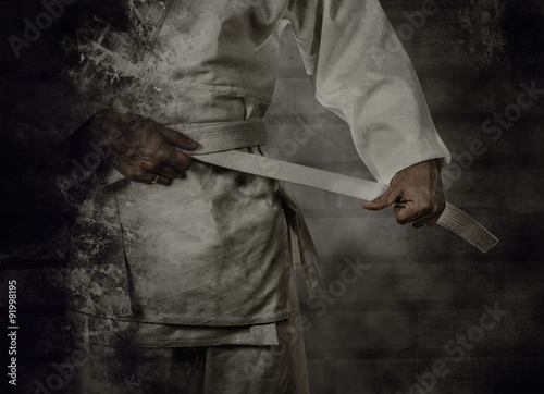 Fotografie, Obraz Karateka tying the white belt (obi) with grunge background