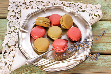 Macaroons on metal plate with raspberries and lavender on wooden background