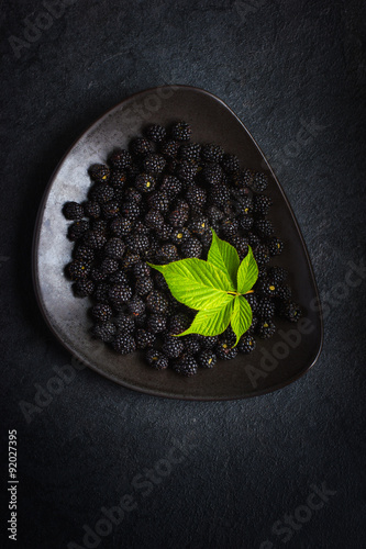Fotografie, Obraz Fresh blackberry and green leaf on black plate