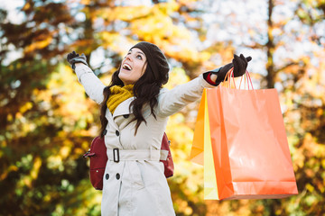 Blissful woman holding shopping bags and having fun buying in autumn rain. Successful female shopper outside in fall season.