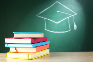 Canvas Print - Stack of books and bachelor hat drawing on blackboard background